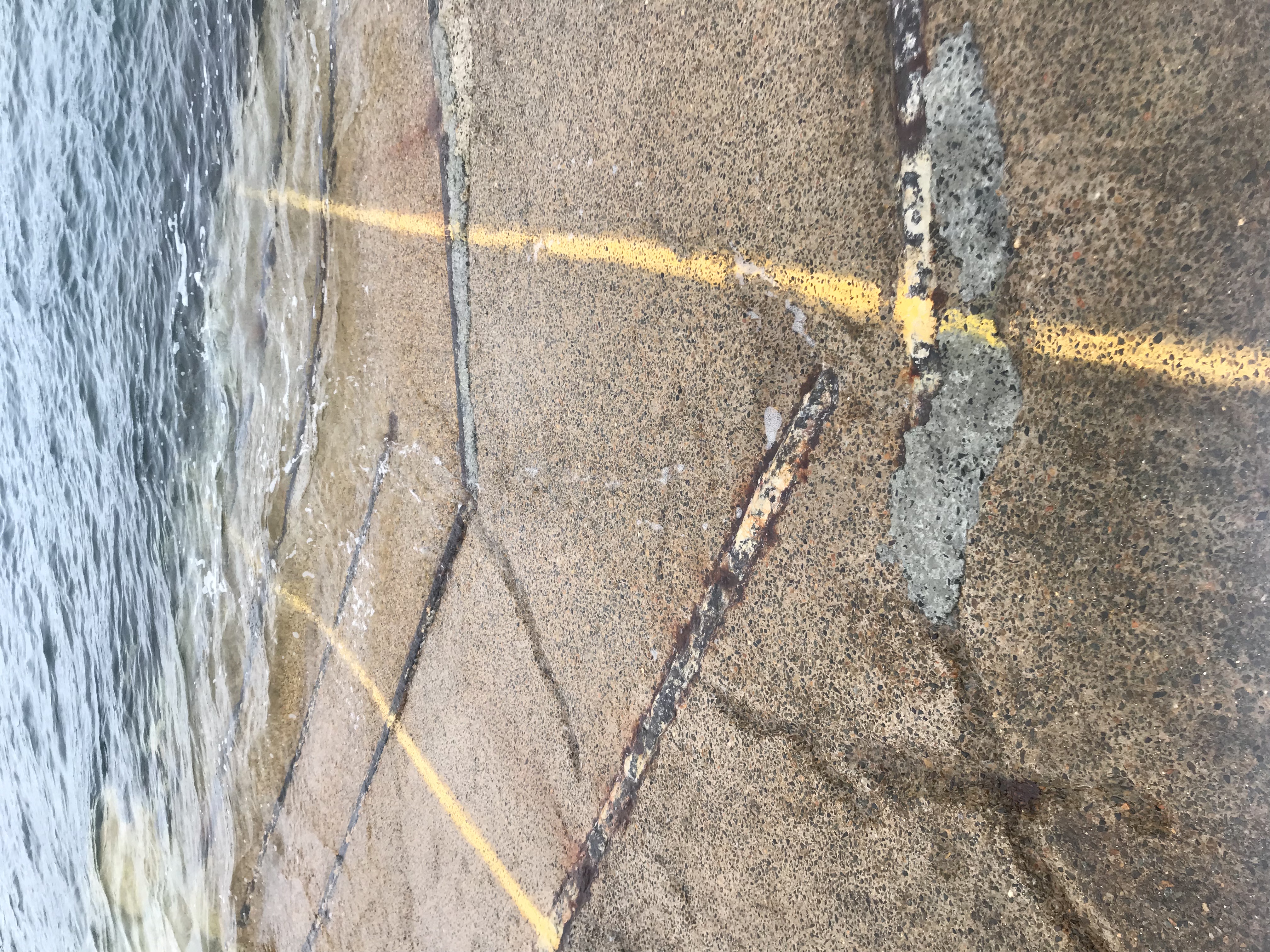 Boat ramp leading into water with some cracks and two yellow lines