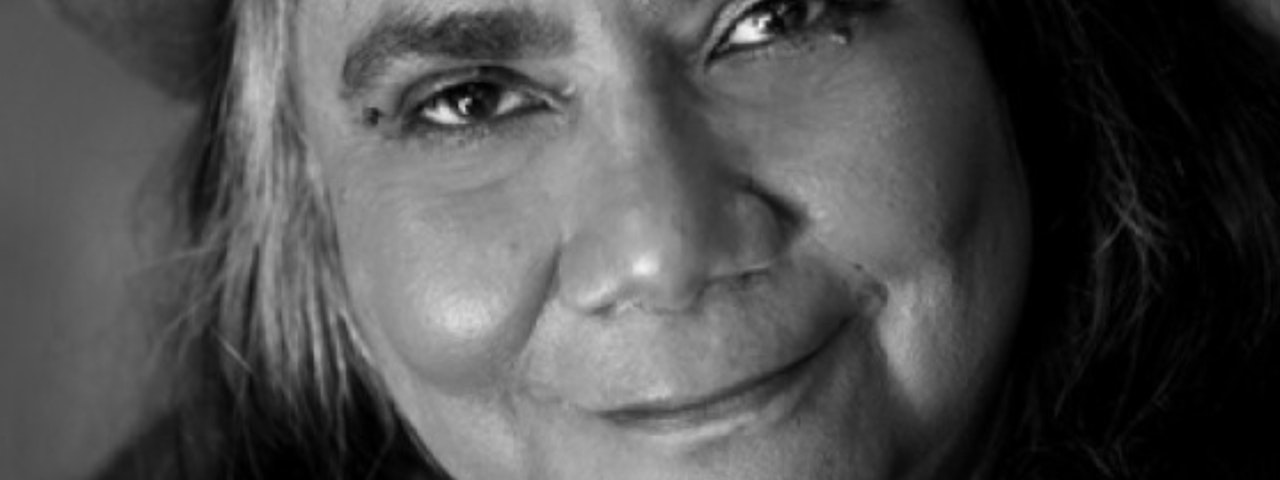 Photograph of Aboriginal woman, close up on her smiling. Can see mouth, nose and eyes and some hair