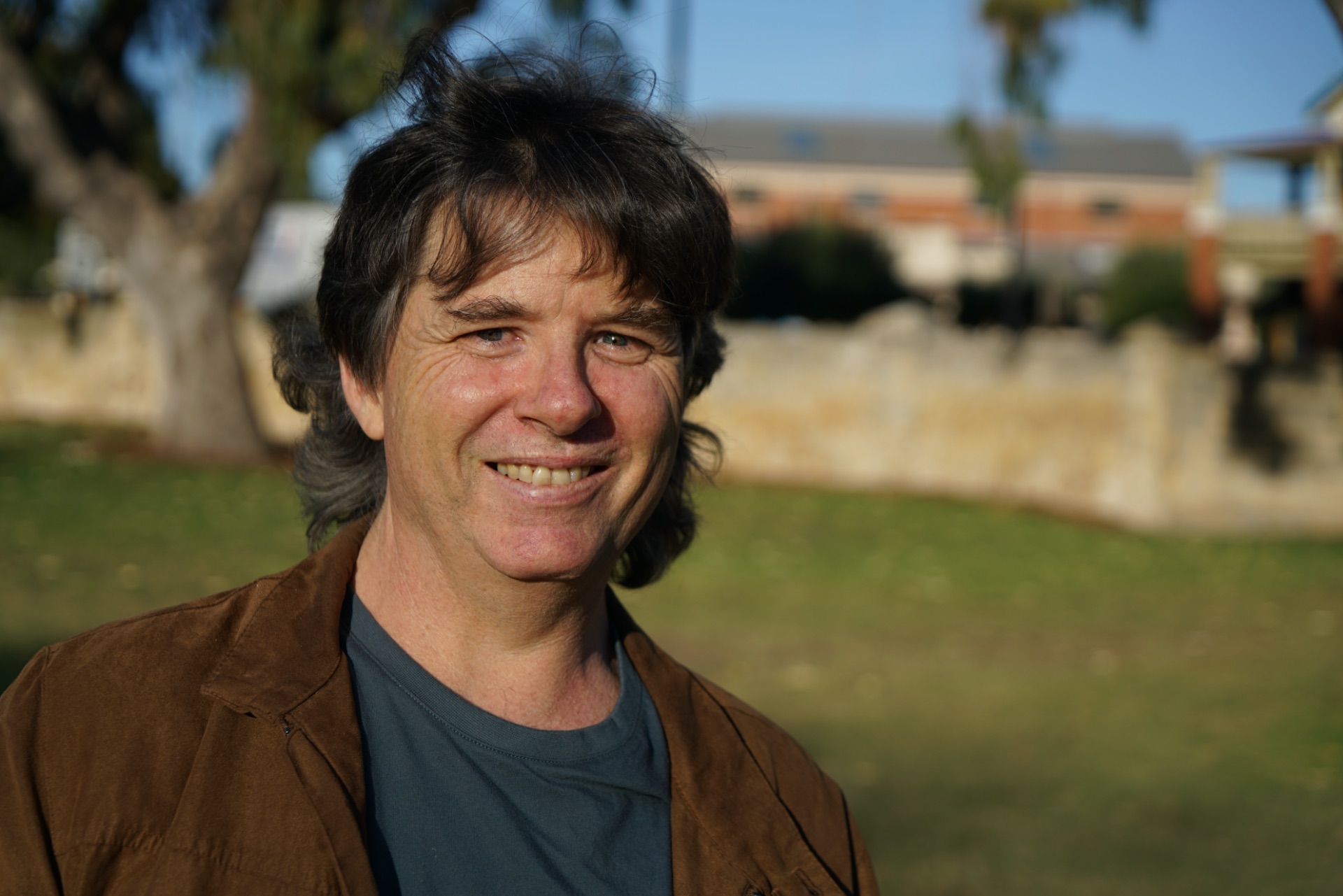 Photo attached description; Man smiling at the camera. He has light skin, brown hair and wears a dark jacket and shirt.